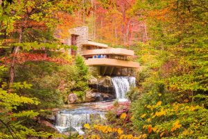 A house in a modern and organic architectural style with a waterfall sits among autumnal trees.